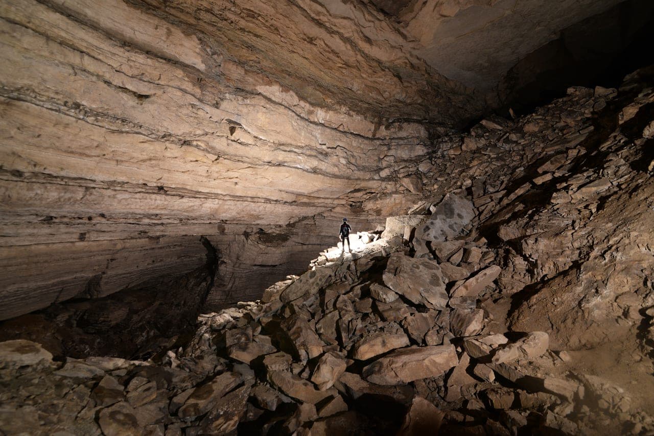 A caver standing in a massive rocky cave chamber
