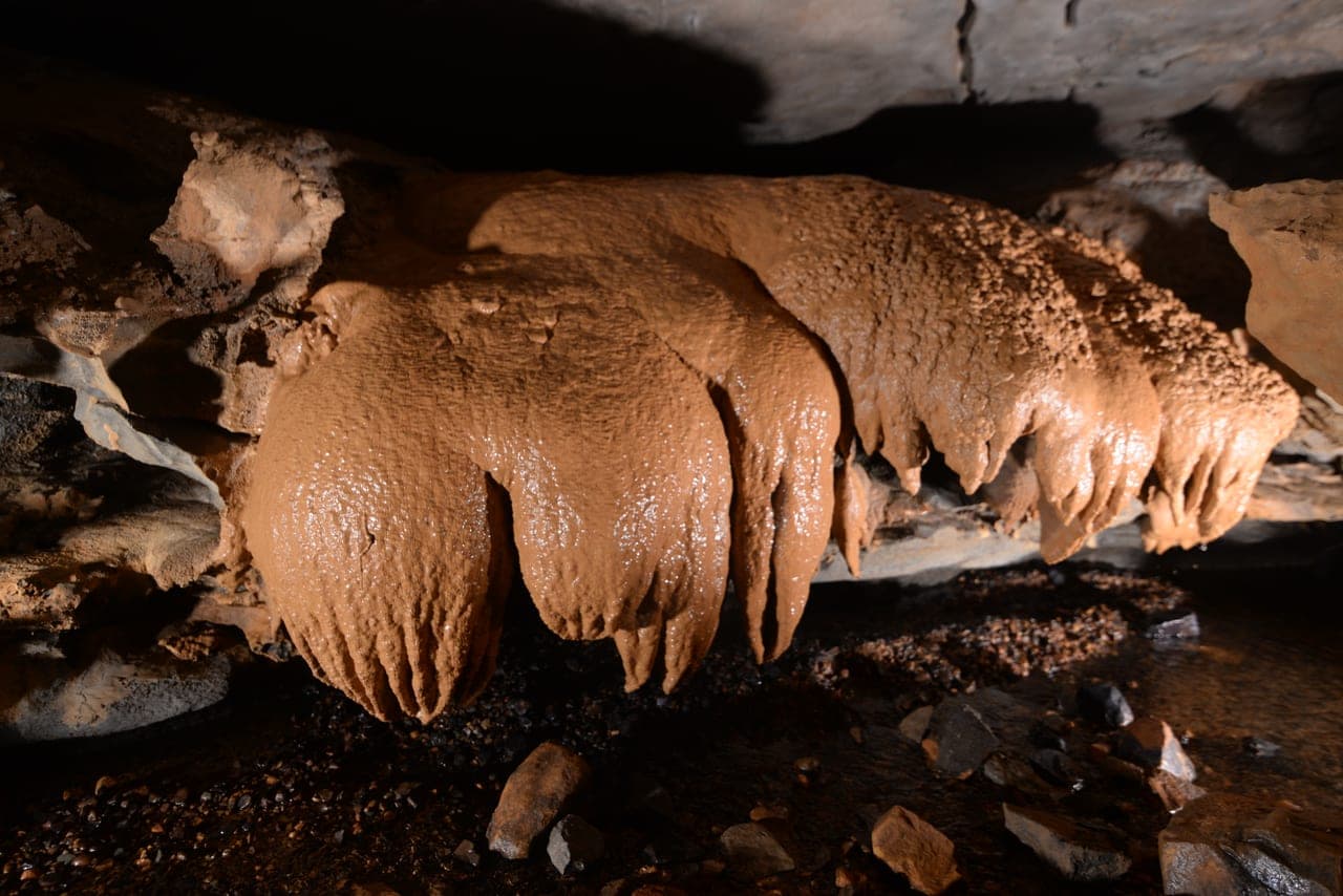 Brown flowstone drapery hanging above cave streambed